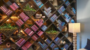 A room with a diamond-patterned bookshelf filled with books, a wooden floor, and a lamp.
