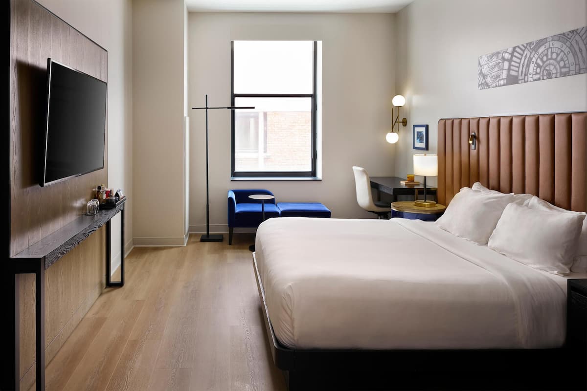 Una habitación de hotel con cama, escritorio, silla, televisión y ventana.