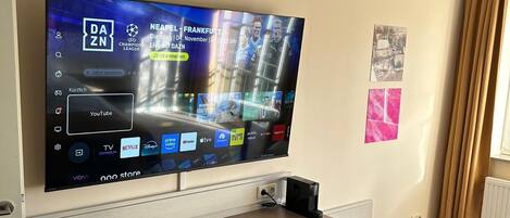 Una habitación de hotel moderna con un televisor de pantalla plana grande montado en la pared, un escritorio de madera con una silla y un radiador.
