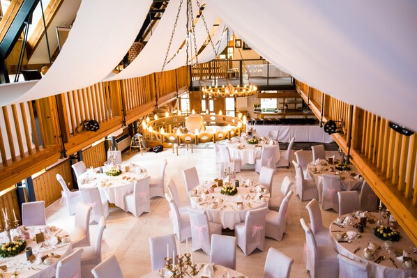 A spacious hall with multiple round tables set for dining, surrounded by white chairs, and a central circular arrangement of tables. - Heide Hotel Reinstorf (Reinstorf)