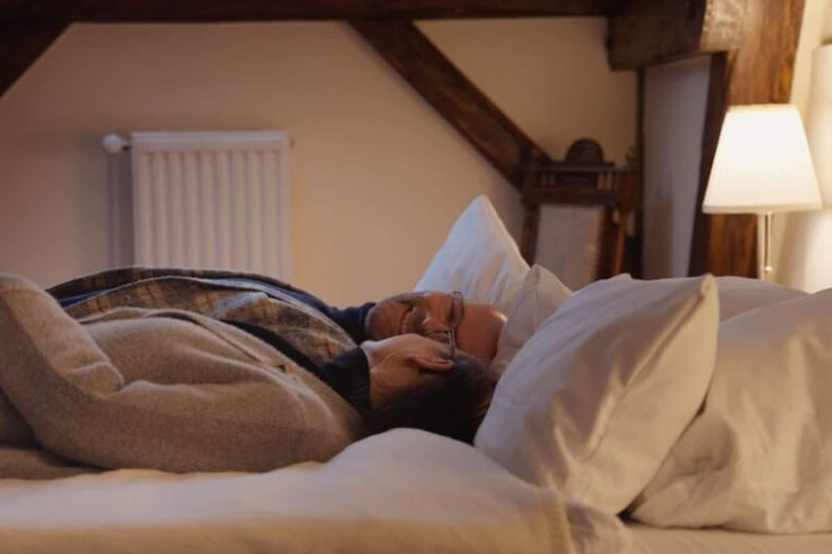 A person lying in bed in a room with exposed wooden beams and a white radiator.