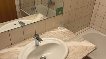 Un baño con lavamanos de mármol, cabina de ducha con mampara de vidrio y bañera.