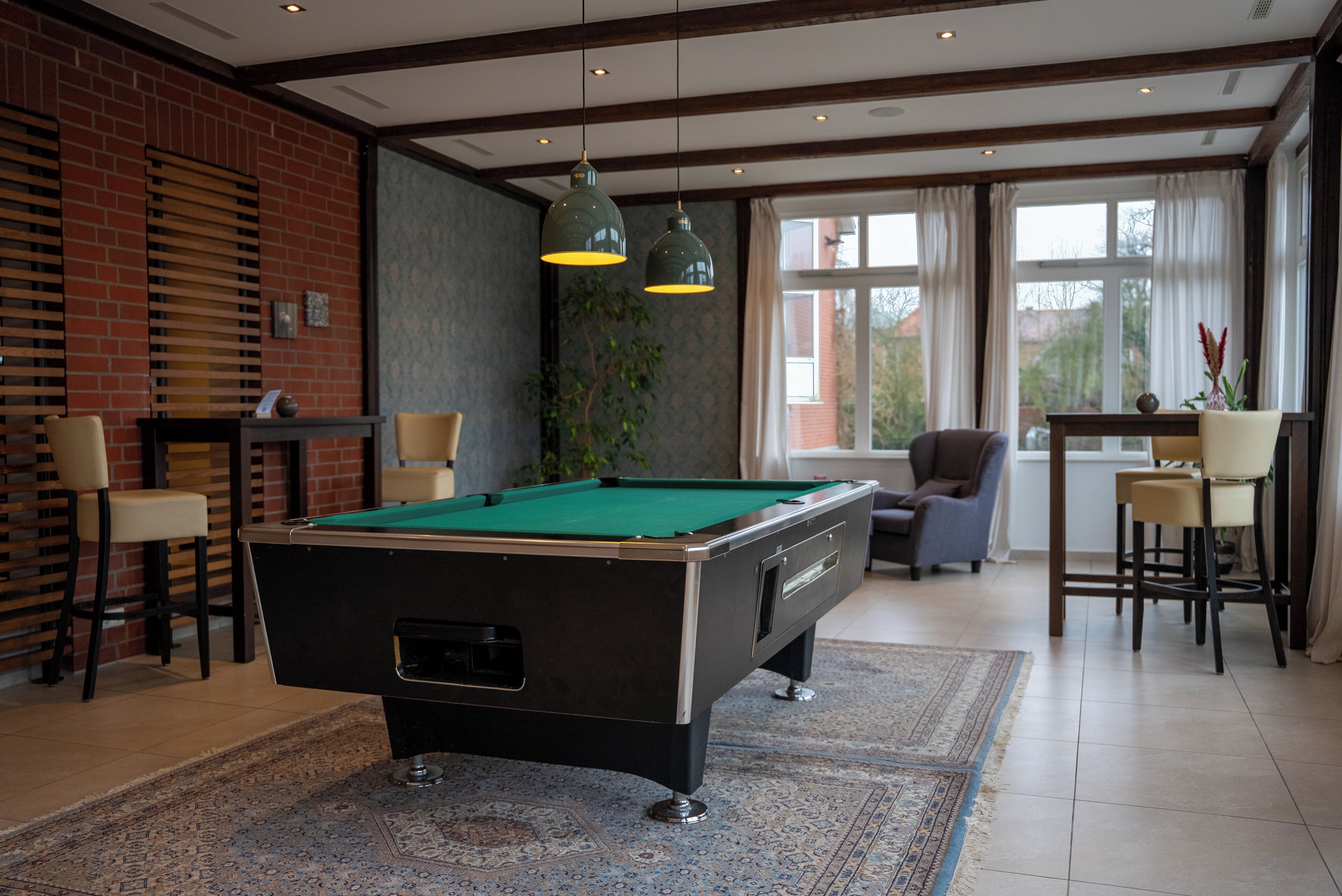 A pool table in a room with a brick wall, wooden ceiling beams, and a large window.
