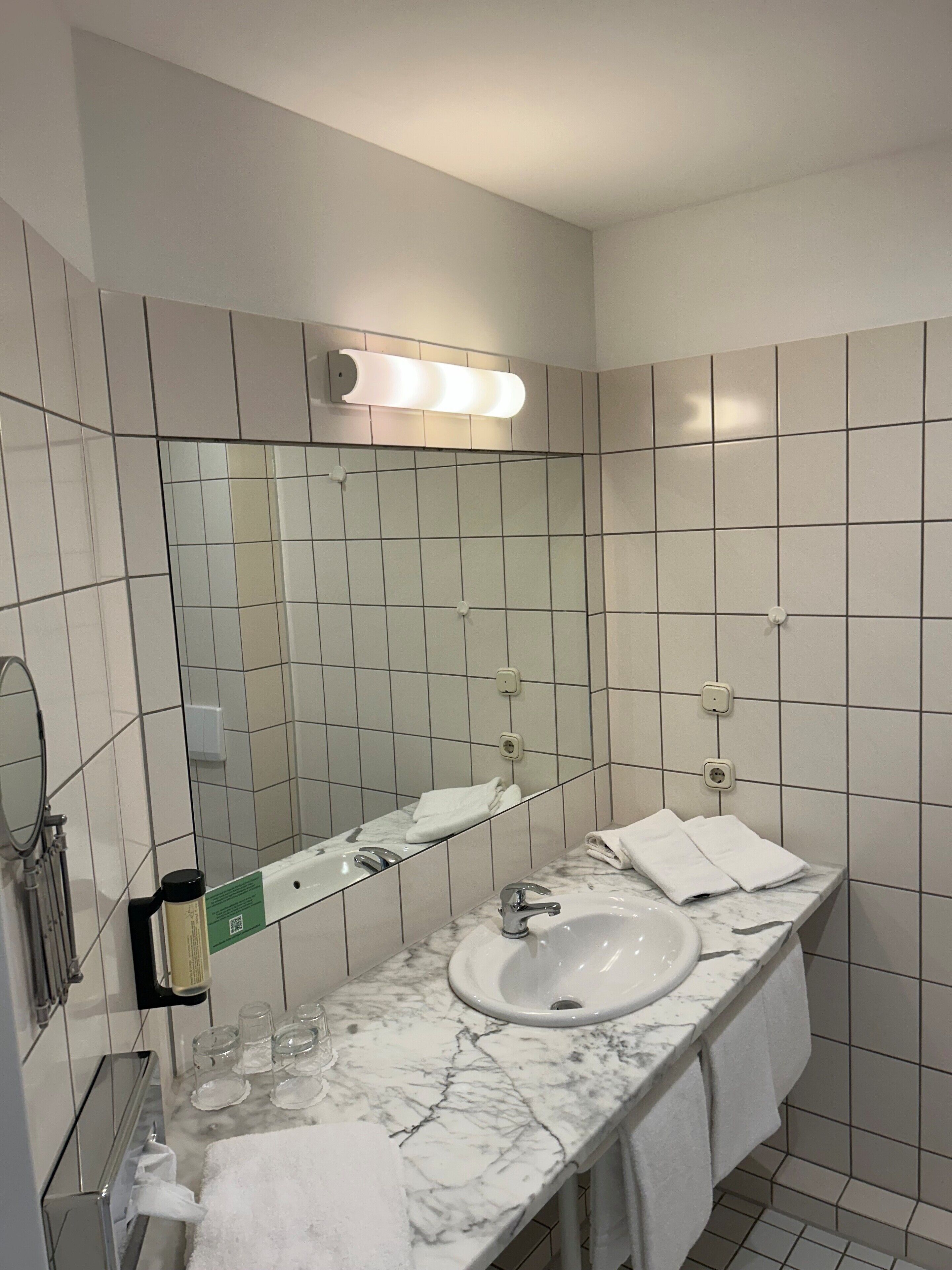 Casa de banho com lavatório branco, espelho e paredes revestidas a azulejos.