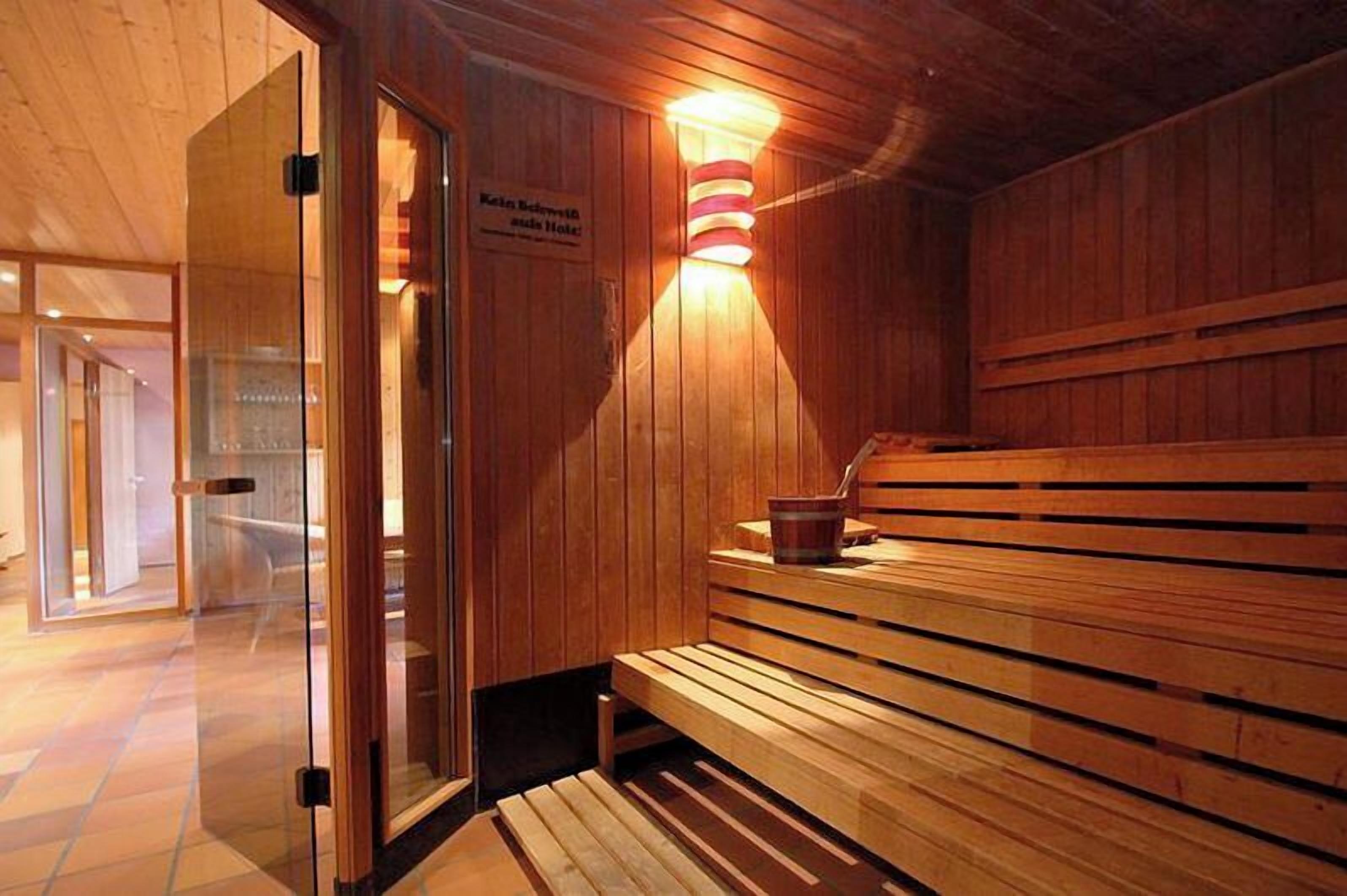 A wooden sauna with benches, a glass door, and a wall-mounted light fixture.