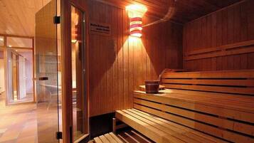 Una sauna de madera con bancos, una puerta de cristal y un aplique de pared.