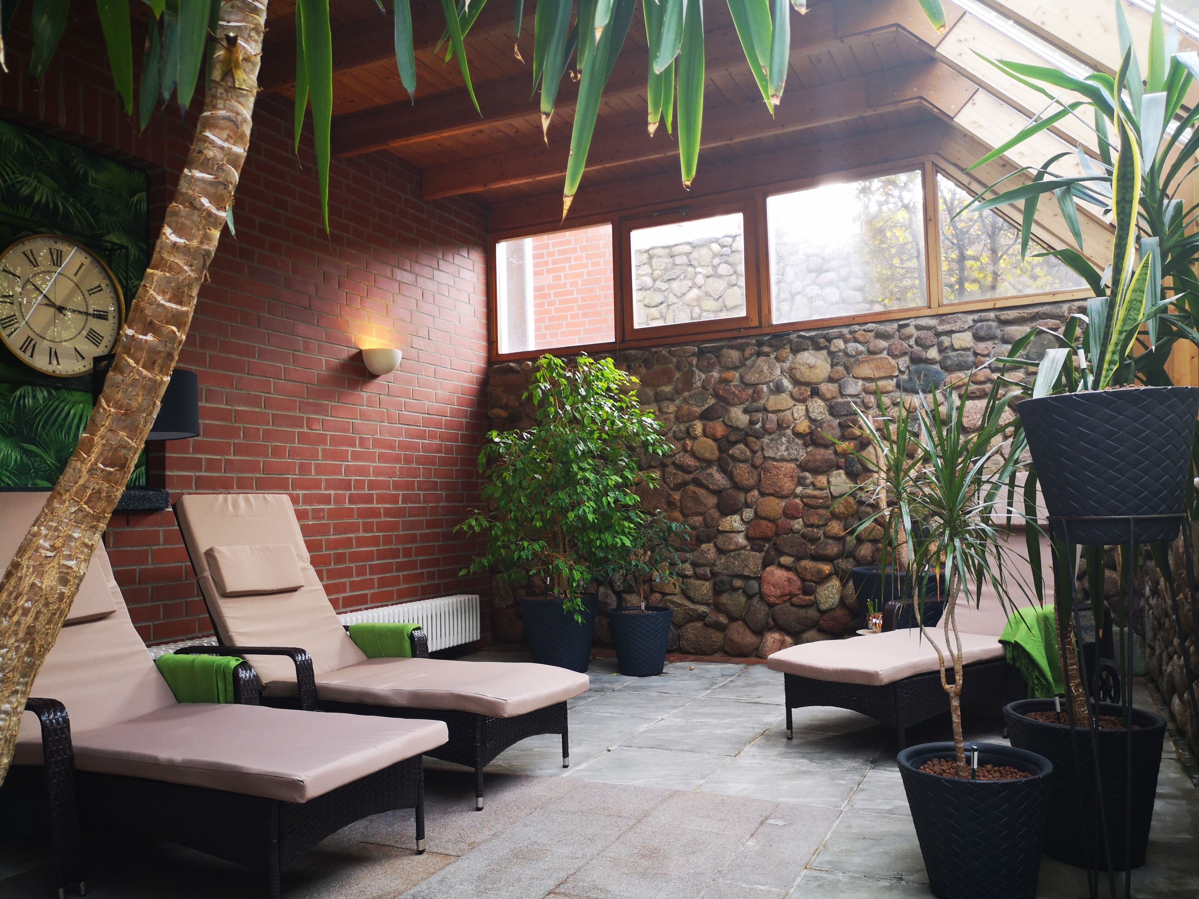 A patio area with lounge chairs, a stone wall, a clock, and potted plants.