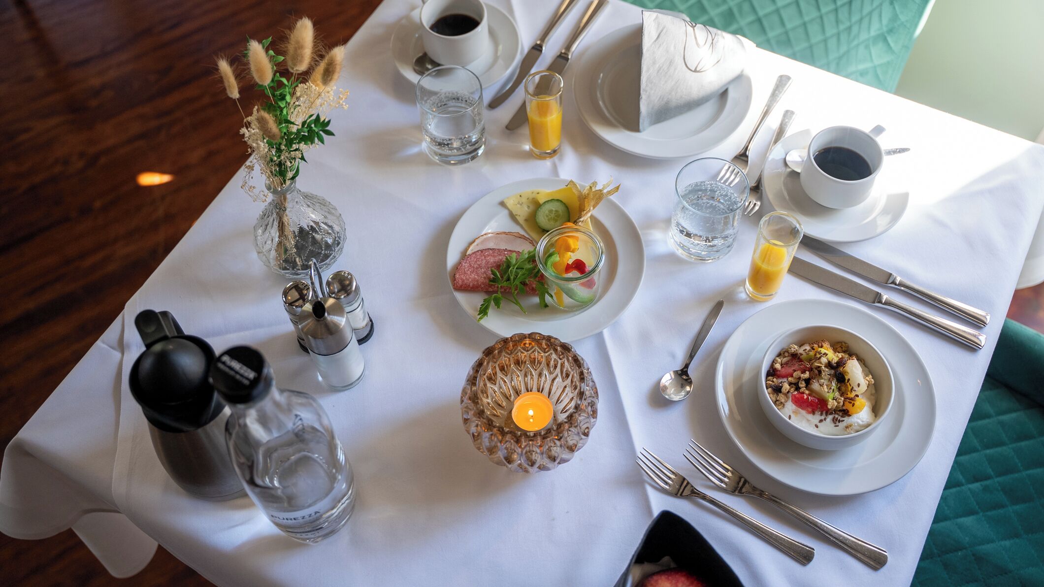 A table set for a meal with plates, cutlery, glasses, and a candle.