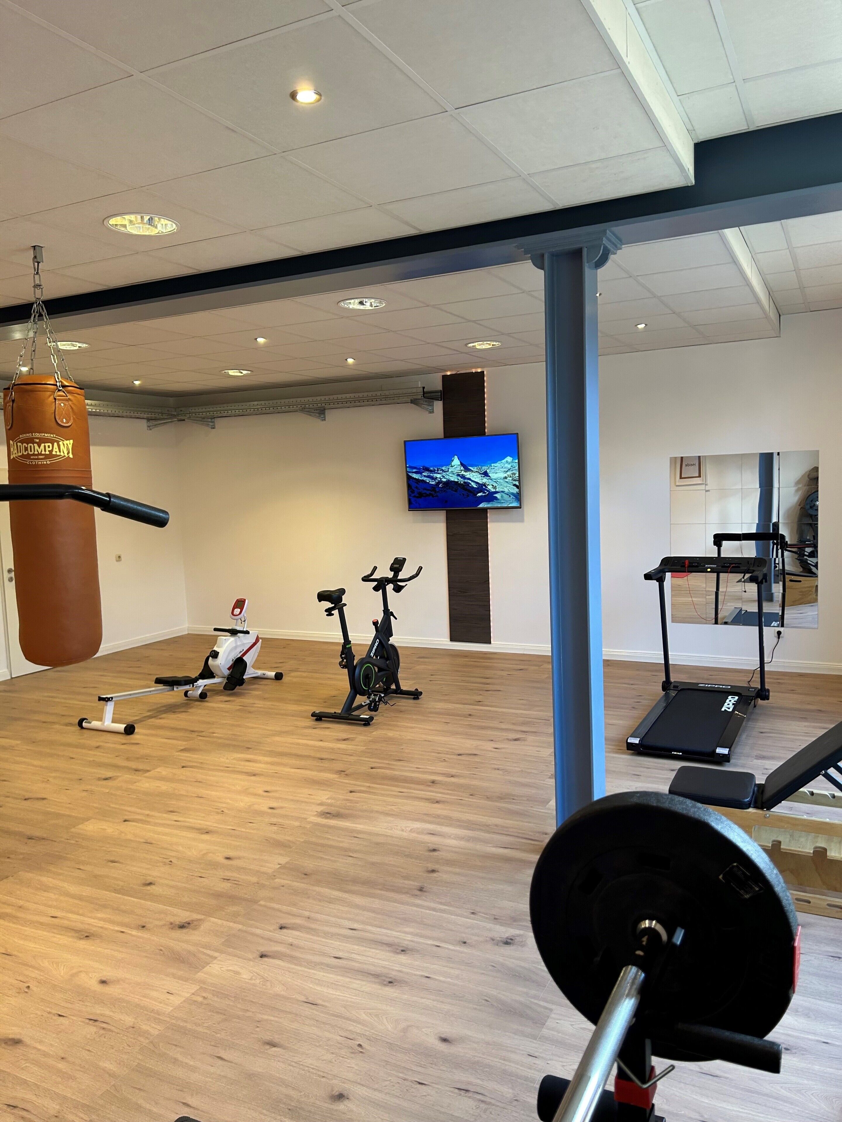 Un gimnasio con equipo de ejercicio, un saco de boxeo y un televisor en la pared.