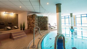 Une piscine avec un mur en pierre, des chaises longues et un sol carrelé.