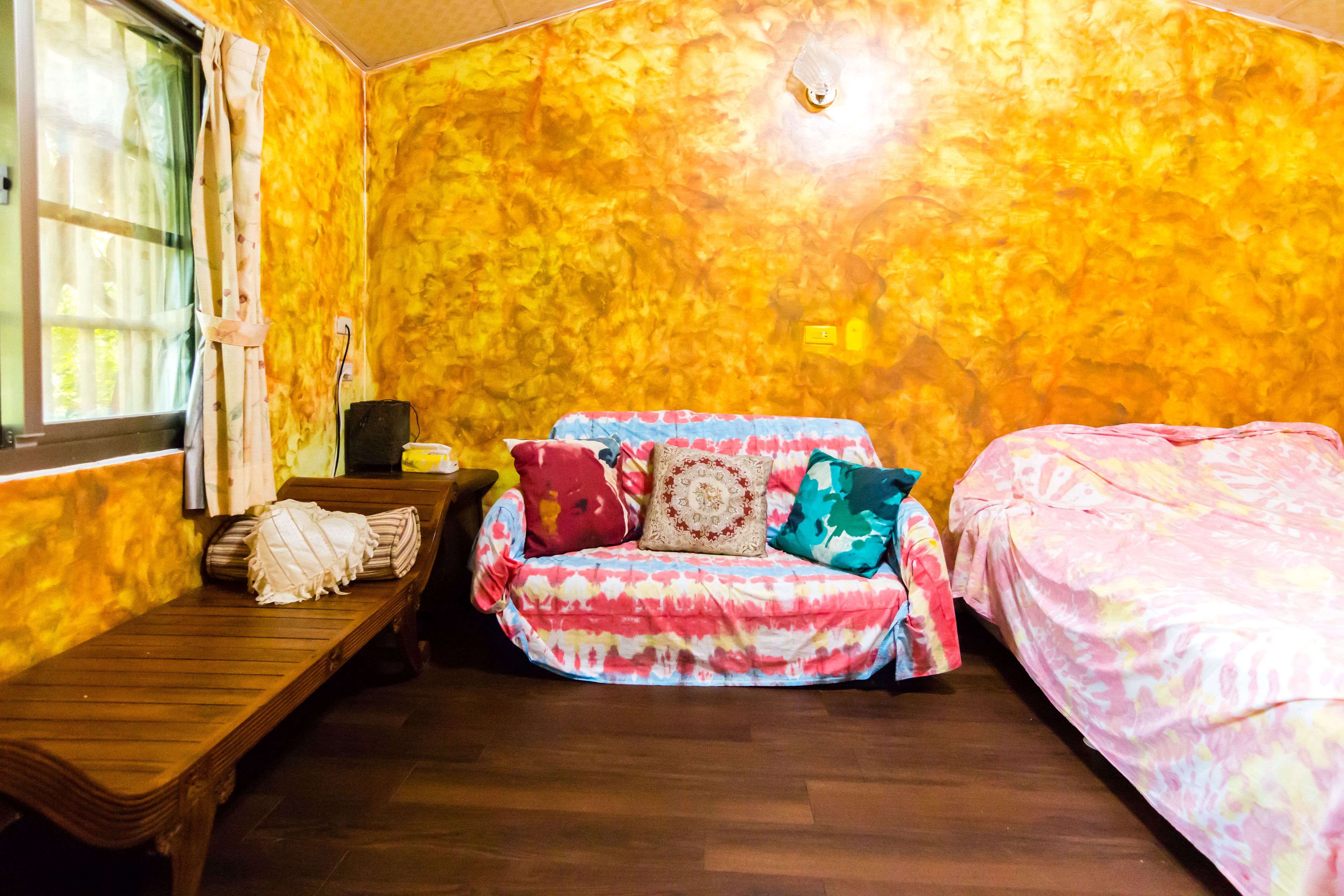 A room with a wooden bench, a colorful sofa with multiple cushions, and a bed with a pink cover.