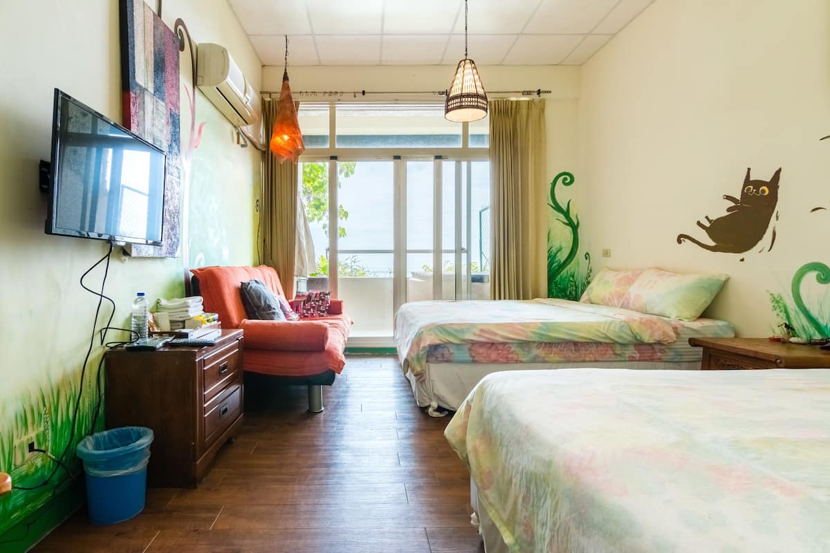 Habitación de hotel con dos camas, televisión, escritorio, silla y ventana con vistas a zonas verdes.
