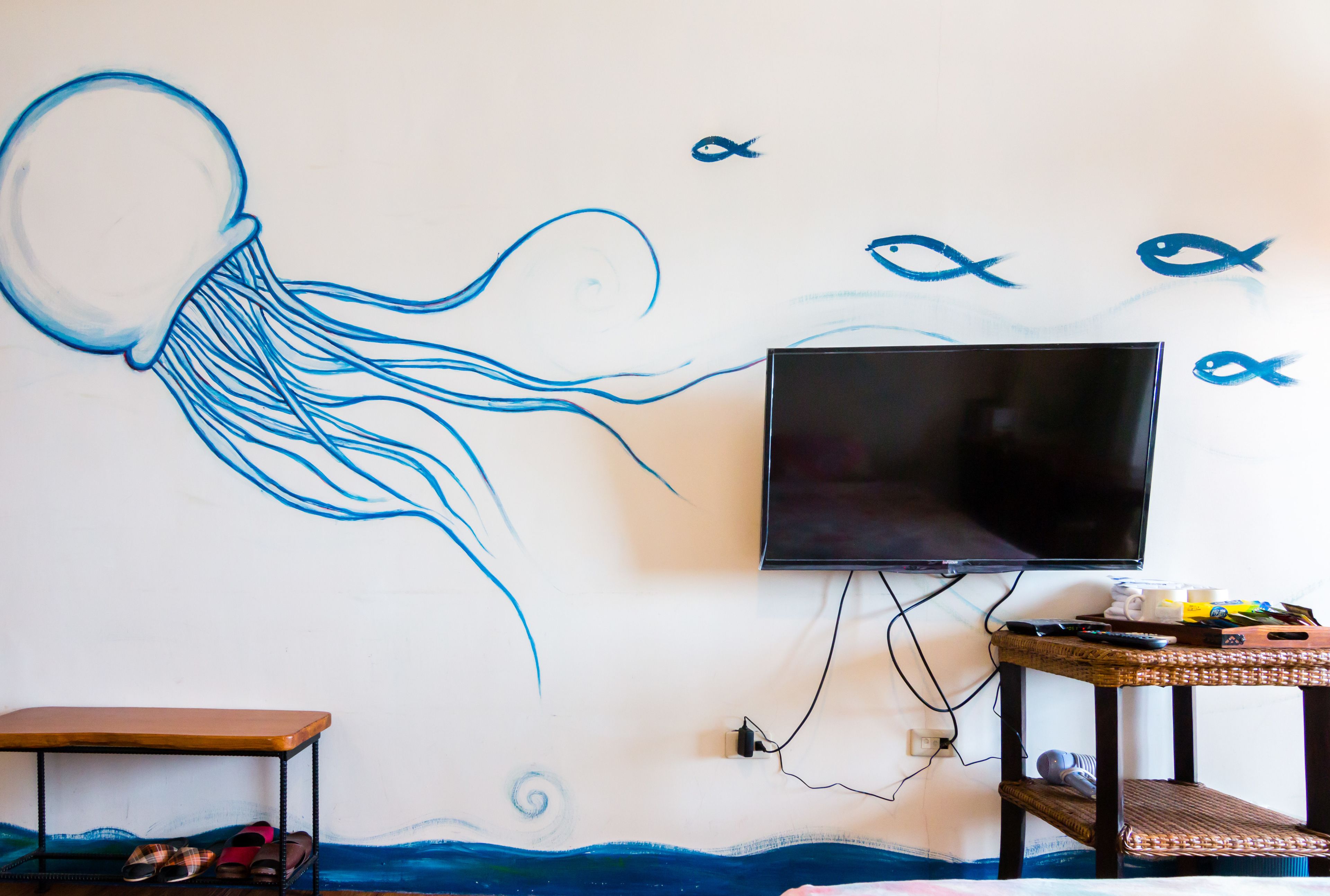 A room with a wall mural of a jellyfish, a television mounted on the wall, a small wooden table, and a bench.
