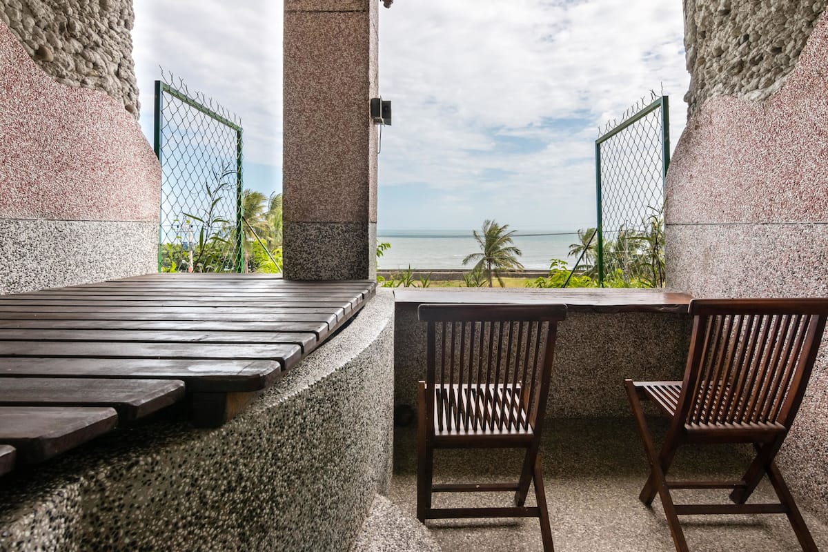 Una terraza con vista al océano, que incluye un banco de madera, dos sillas de madera y un muro de piedra.