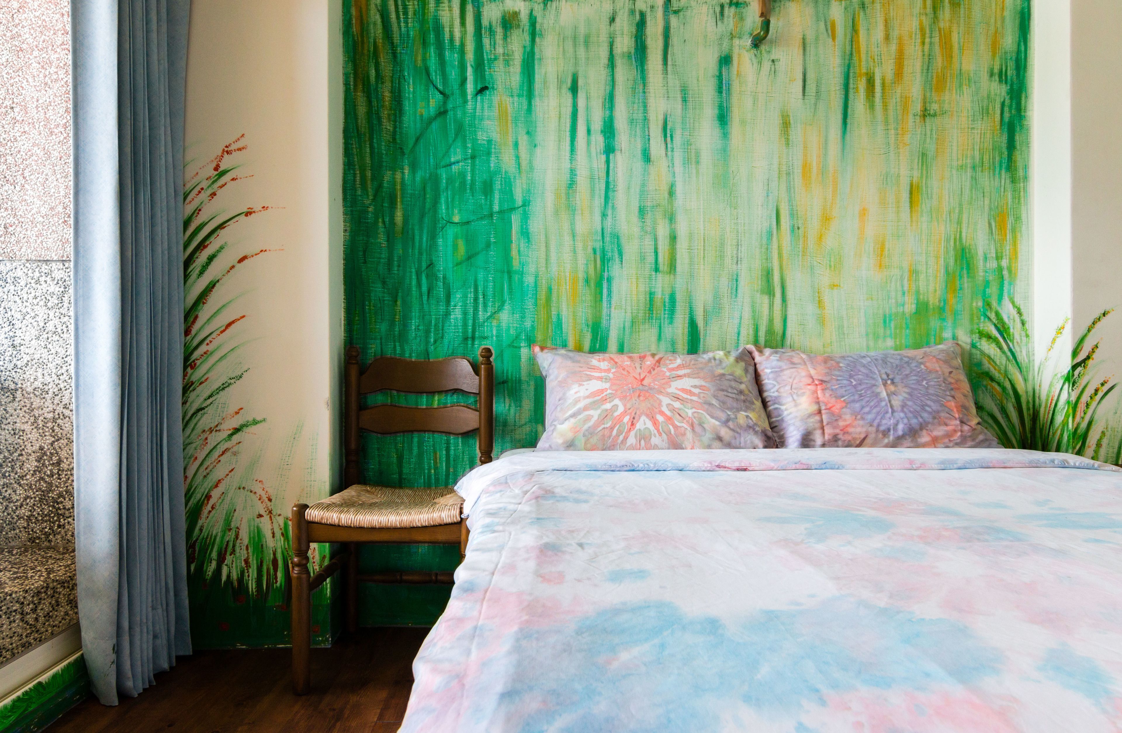 A bedroom with a bed, a chair, and a green wall with a textured pattern.