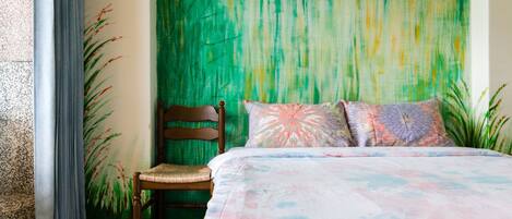 A bedroom with a bed, a chair, and a green wall with a textured pattern.