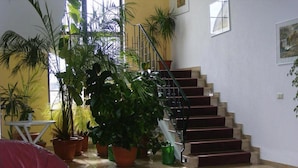 A spacious living area with a red leather sofa, a round coffee table, and multiple potted plants. A staircase with a red carpet leads to an upper level. - Hotel Schwartze (Weimar)