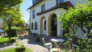 A building with a white facade, arched windows, and a tiled roof. There is a paved patio with outdoor furniture and potted plants. - Hotel Schwartze (Weimar)