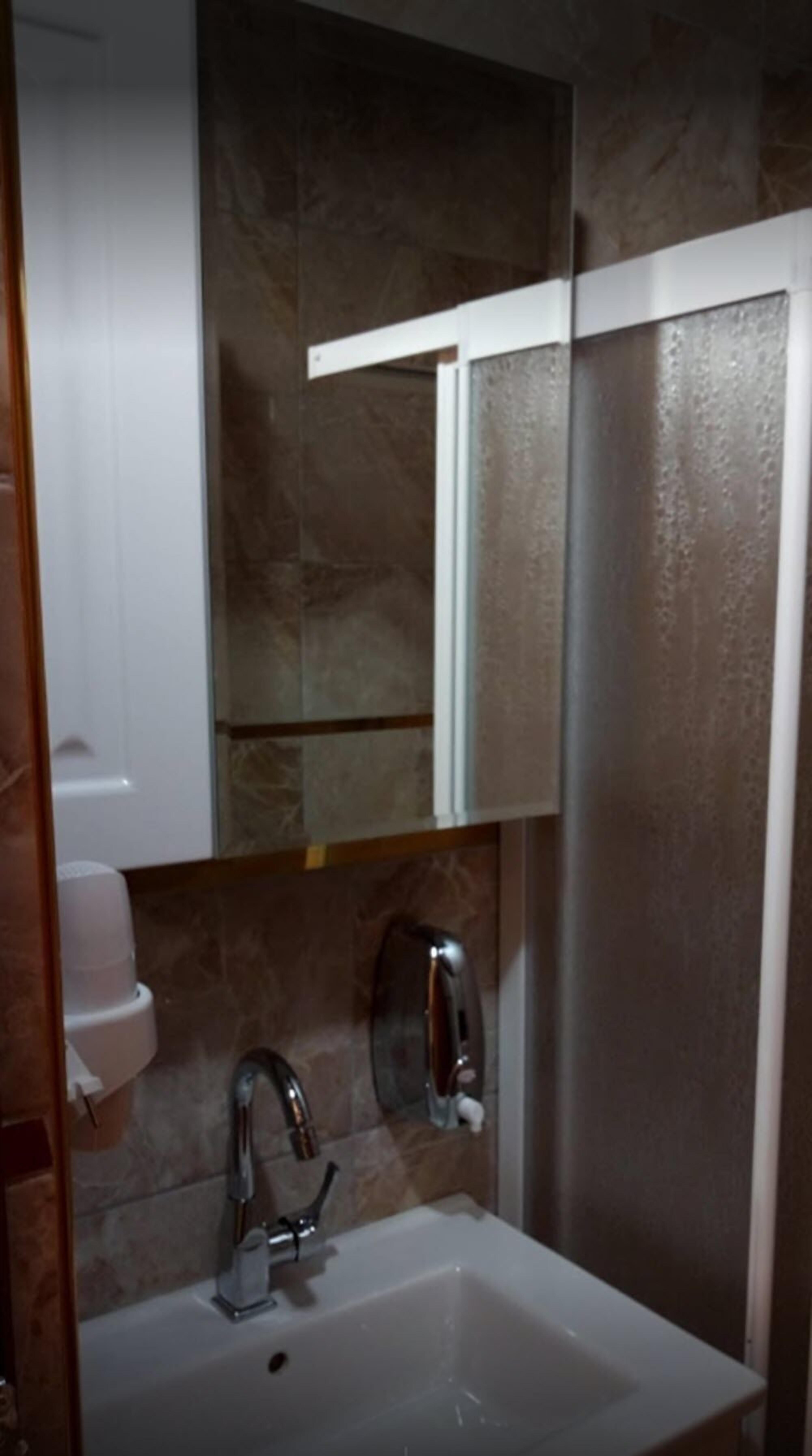A bathroom with a white sink, a mirror, and a soap dispenser.