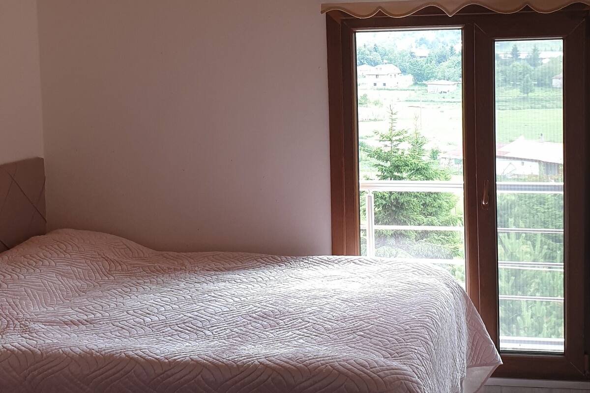 Ein Schlafzimmer mit einem Bett, einem Fenster mit Blick auf Grünflächen und einer Holzbalkendecke.
