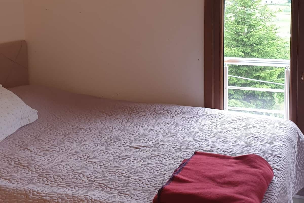 Ein Schlafzimmer mit Bett, Fenster und Blick ins Grüne.