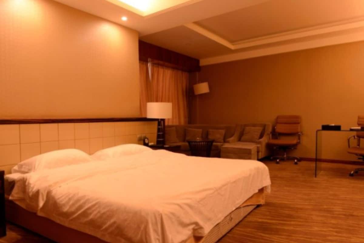 A hotel room with a large bed, a desk, a chair, and a lamp.