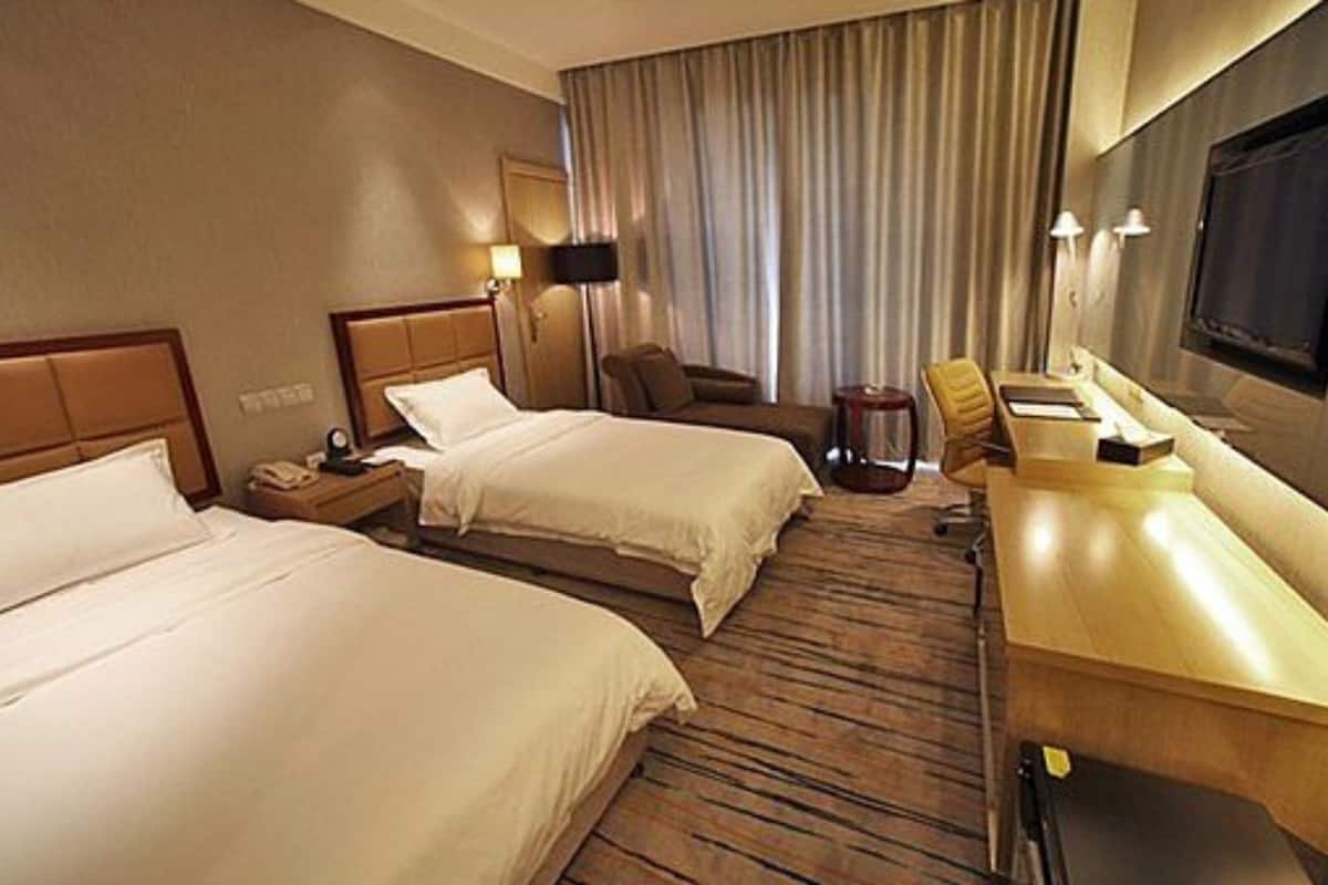 A hotel room with two beds, a desk, a chair, a lamp, and a TV.