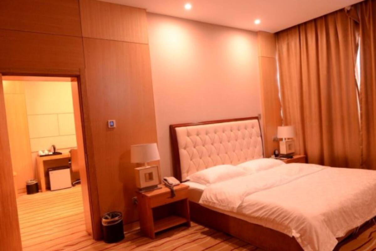 A hotel room with a large bed, wooden flooring, a nightstand with a lamp, and a door leading to another room.