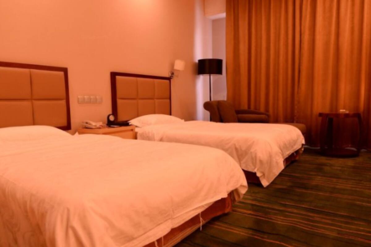 A hotel room with two beds, a chair, a lamp, and a small table.