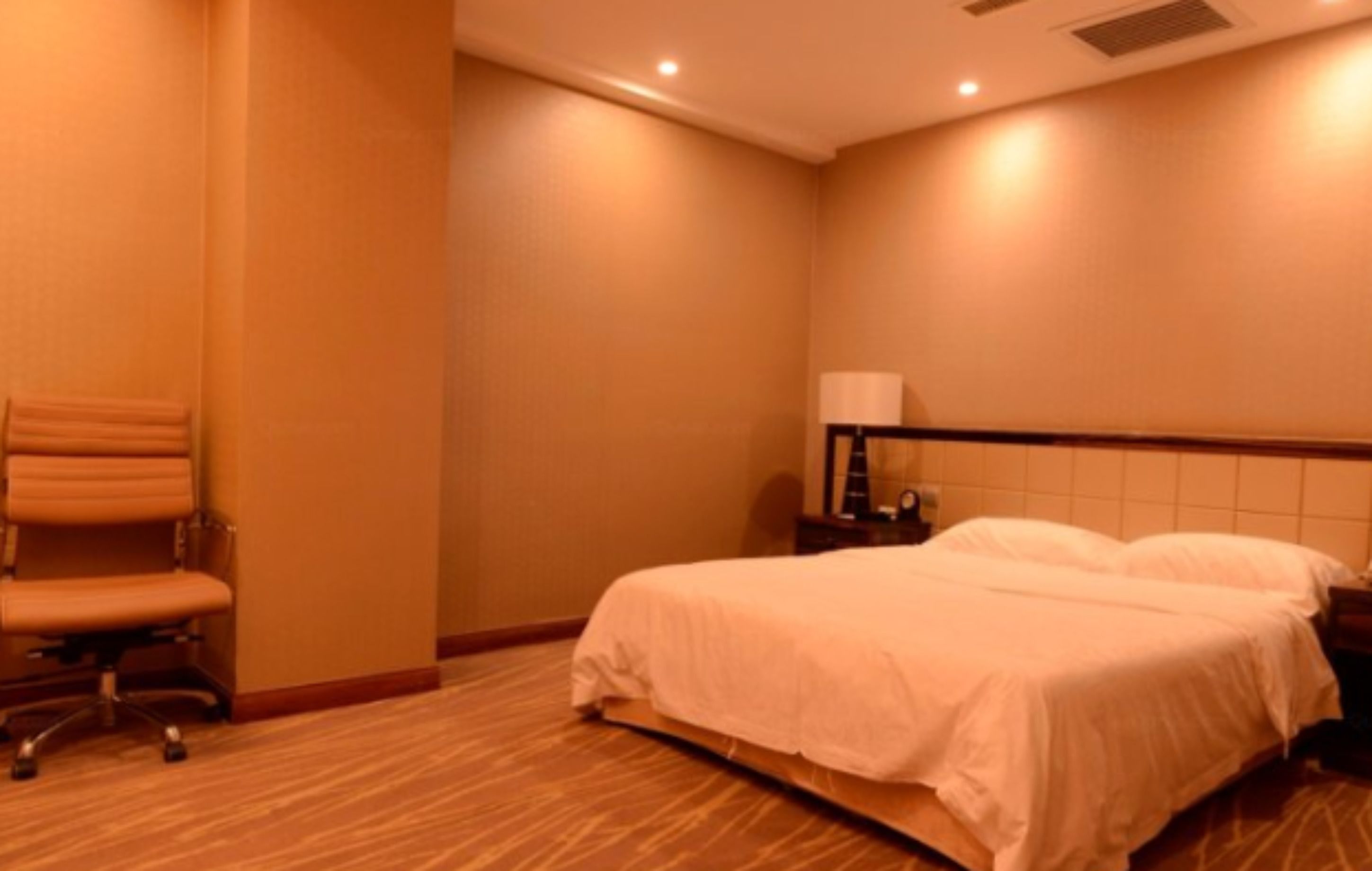A hotel room with a bed, a chair, a nightstand, and a lamp.
