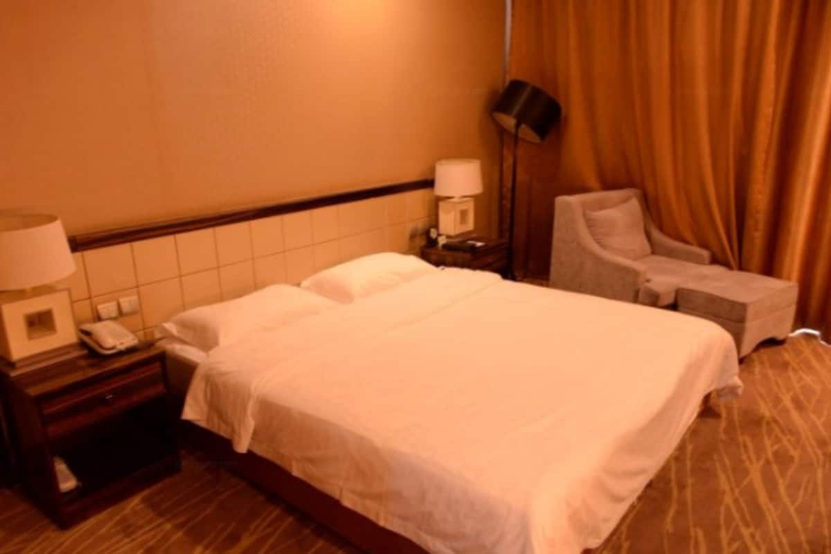 A hotel room with a bed, a chair, a nightstand with a lamp, and a telephone.