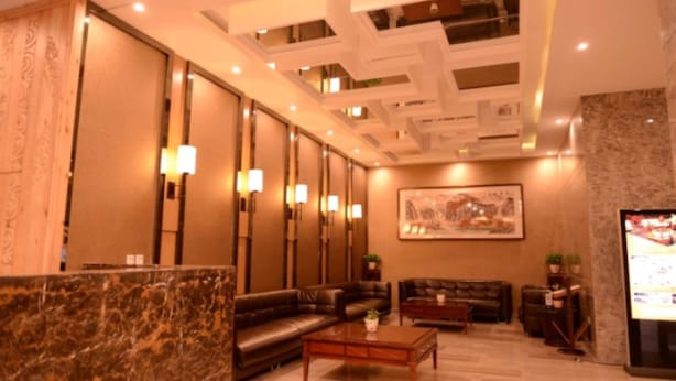 A spacious lobby with a marble reception desk, leather sofas, a coffee table, and a large painting on the wall.