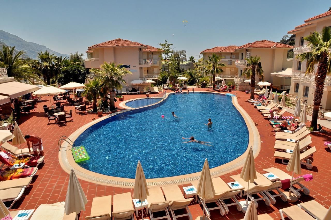 Ein Swimmingpool, umgeben von Liegestühlen und Sonnenschirmen, mit Palmen und einem Berg im Hintergrund.