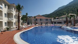 A swimming pool surrounded by lounge chairs and palm trees, with a mountain in the background. - The Blue Lagoon Deluxe Hotel (Fethiye)