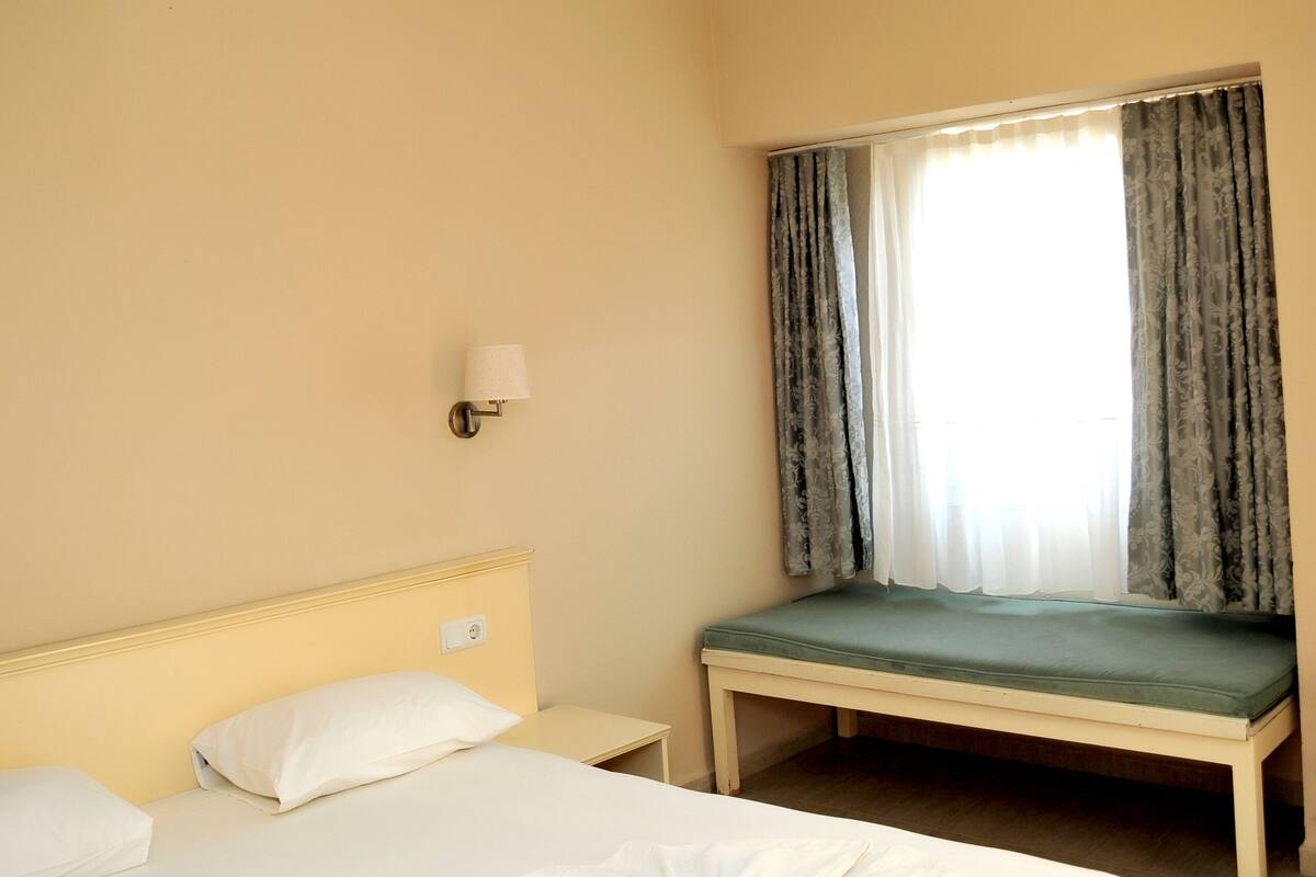 Hotellihuone, jossa on sänky, yöpöytä, lamppu ja ikkuna, jossa on verhot.