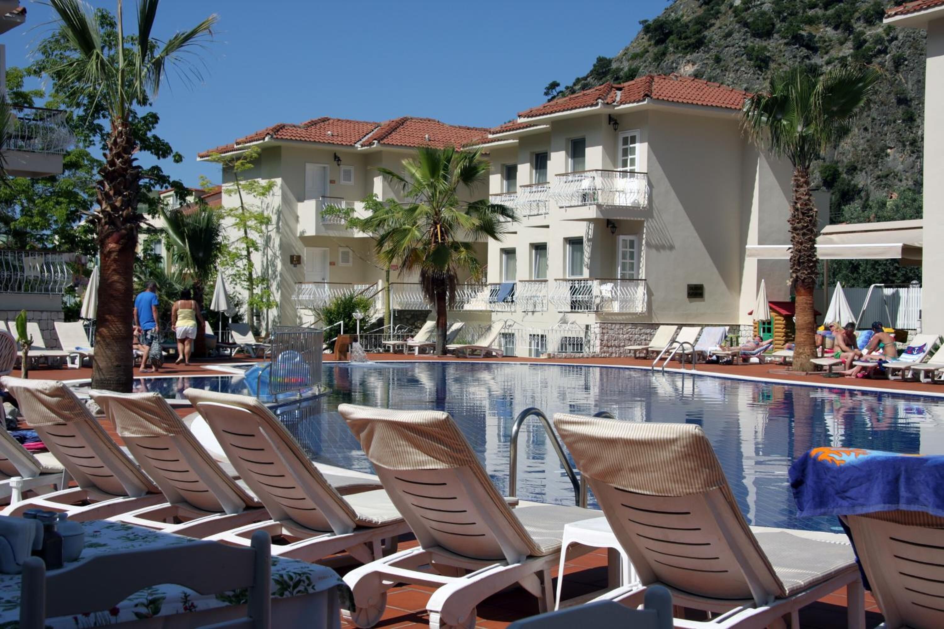 Un área junto a la piscina con sillones, una pileta y un edificio con balcones.