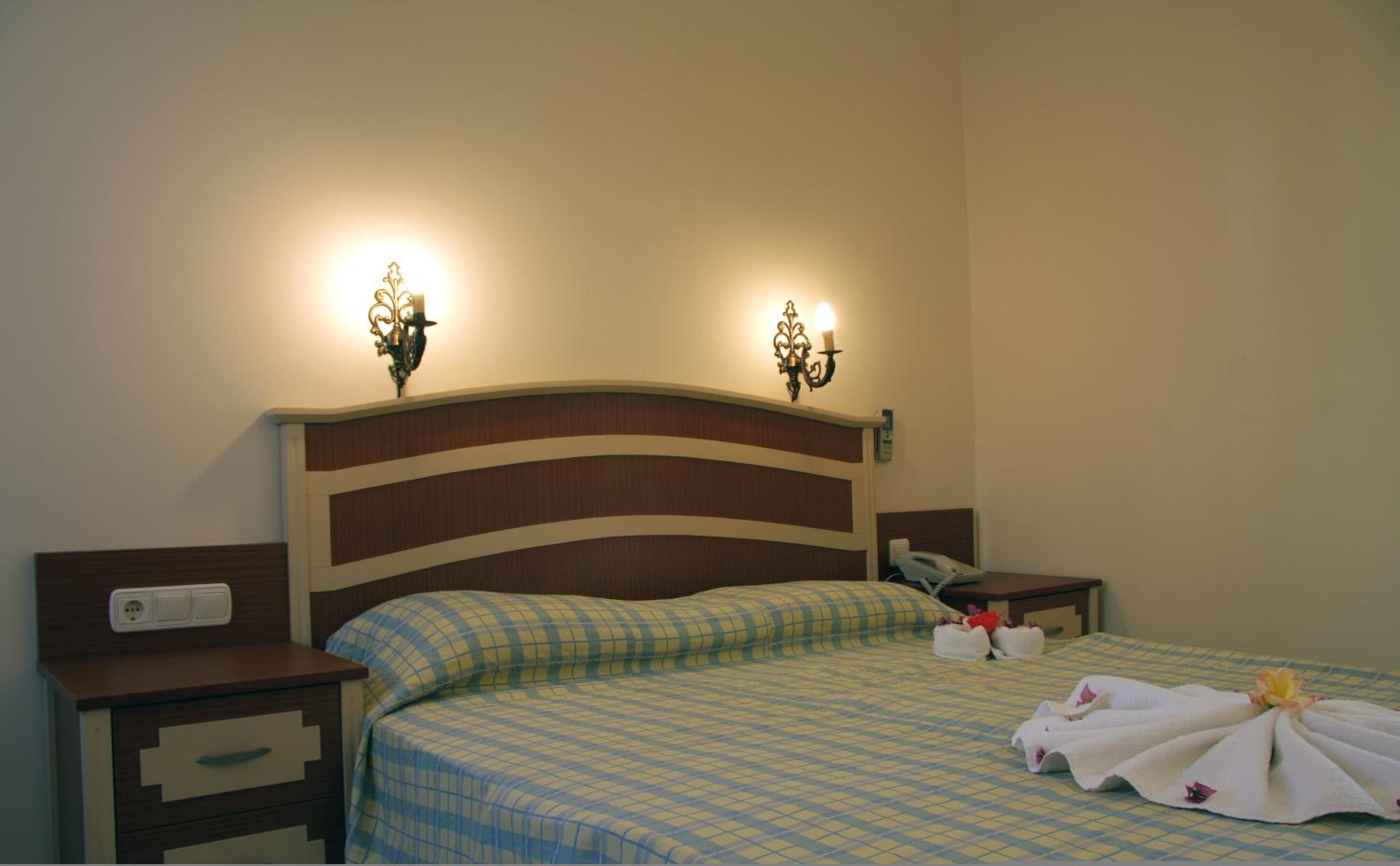 Una habitación de hotel con cama, mesitas de noche y lámparas de pared.