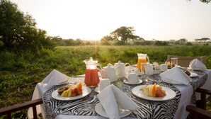 An outdoor dining table set with breakfast items, surrounded by lush greenery and trees.