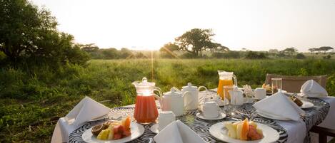 An outdoor dining table set with breakfast items, surrounded by lush greenery and trees.