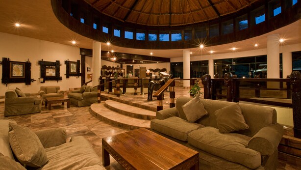 A spacious lobby with a high ceiling, a central staircase, and a seating area with sofas and a coffee table.