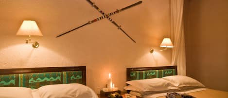 A hotel room with two beds, each with a headboard, a nightstand with a candle, and a wall-mounted lamp.