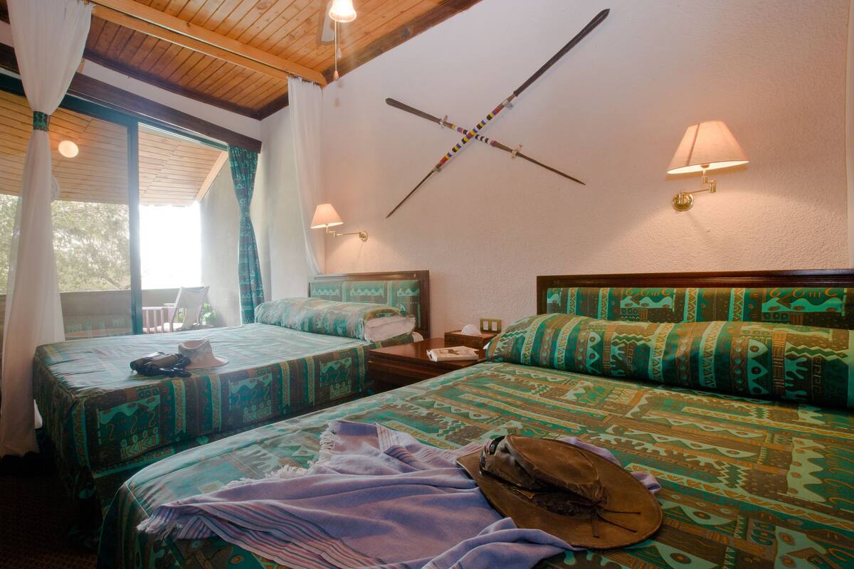 Una habitación con dos camas, techo de madera y un esquiercross montado en la pared.