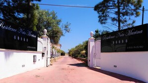 Uma entrada fechada com placas indicando 'Residence Noto Marina', céu claro e um caminho que leva a uma propriedade.