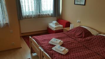 A hotel room with a bed, a red chair, a small table, and a window with curtains.