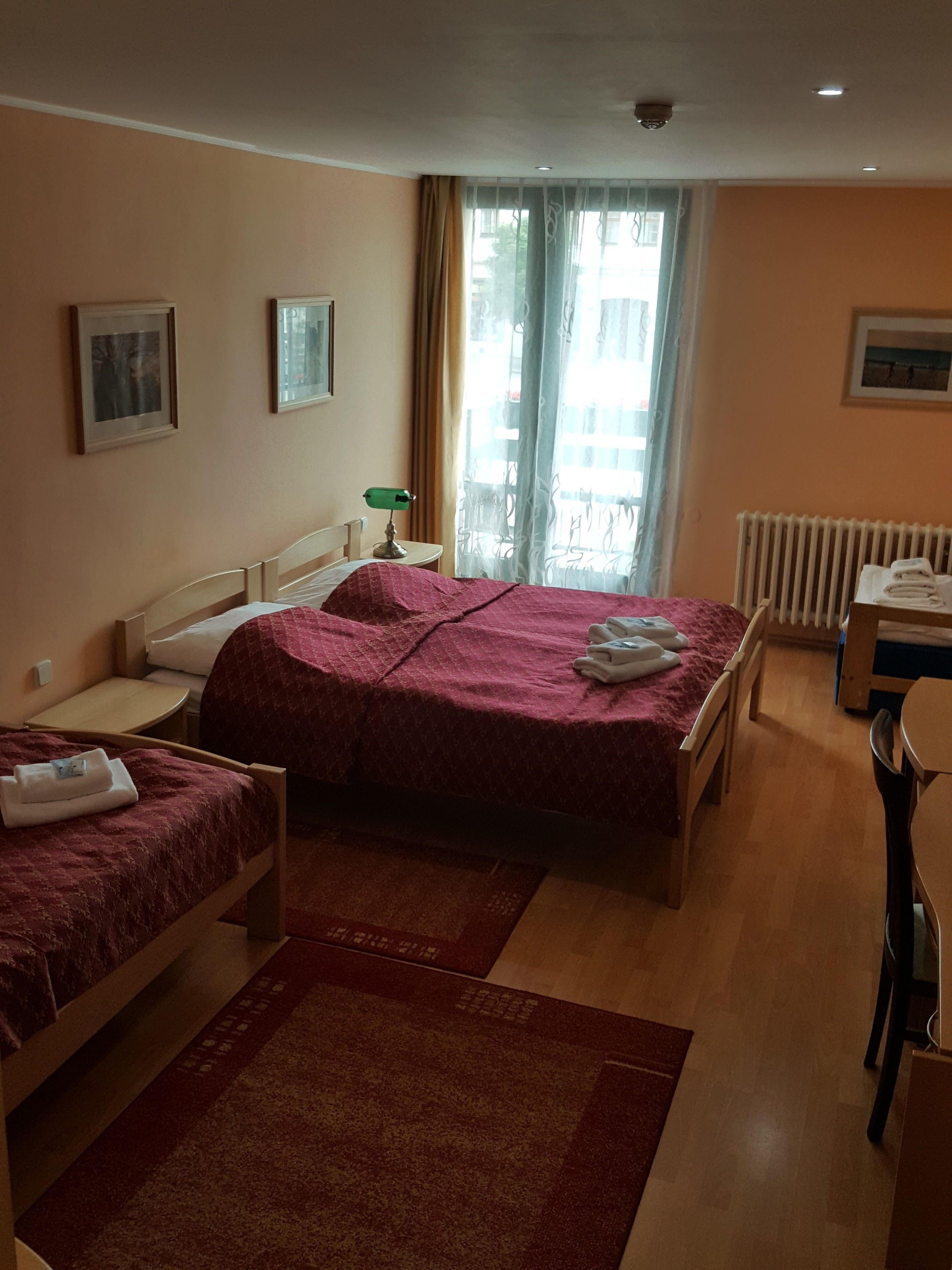 Una habitación de hotel con dos camas, un escritorio, una silla, un radiador y una ventana con cortinas.