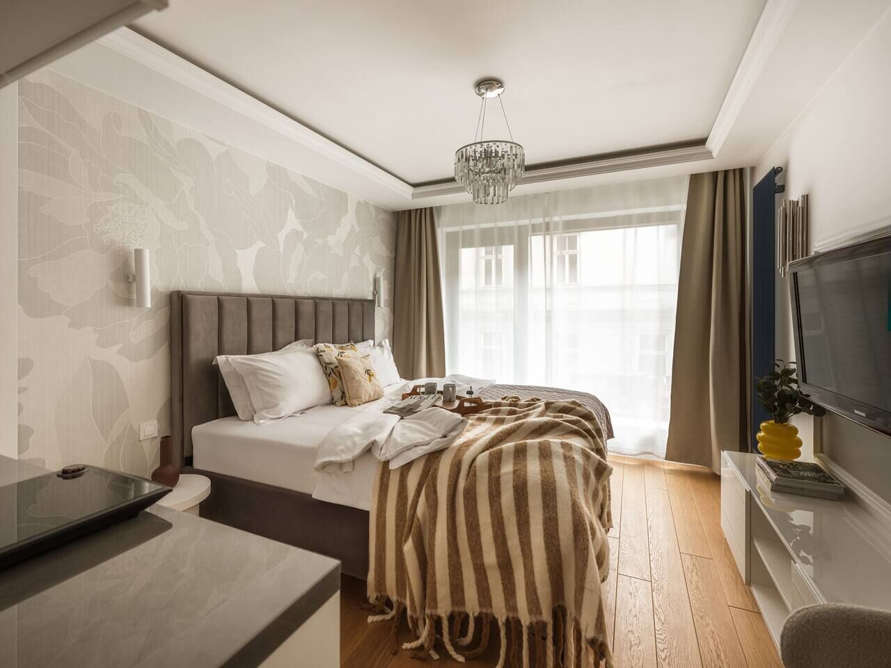 A hotel room with a bed, a TV, a desk, and a window with curtains.