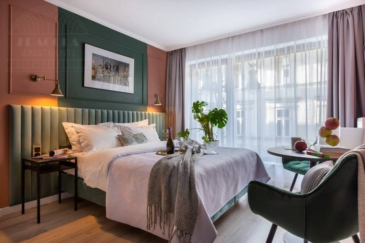 Ein modernes Hotelzimmer mit Bett, Nachttisch, Lampe und Blick auf die Stadt durch große Fenster.