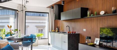 A modern kitchen with a built-in oven, a dining area with a table and chairs, and a large window providing a view of the city.