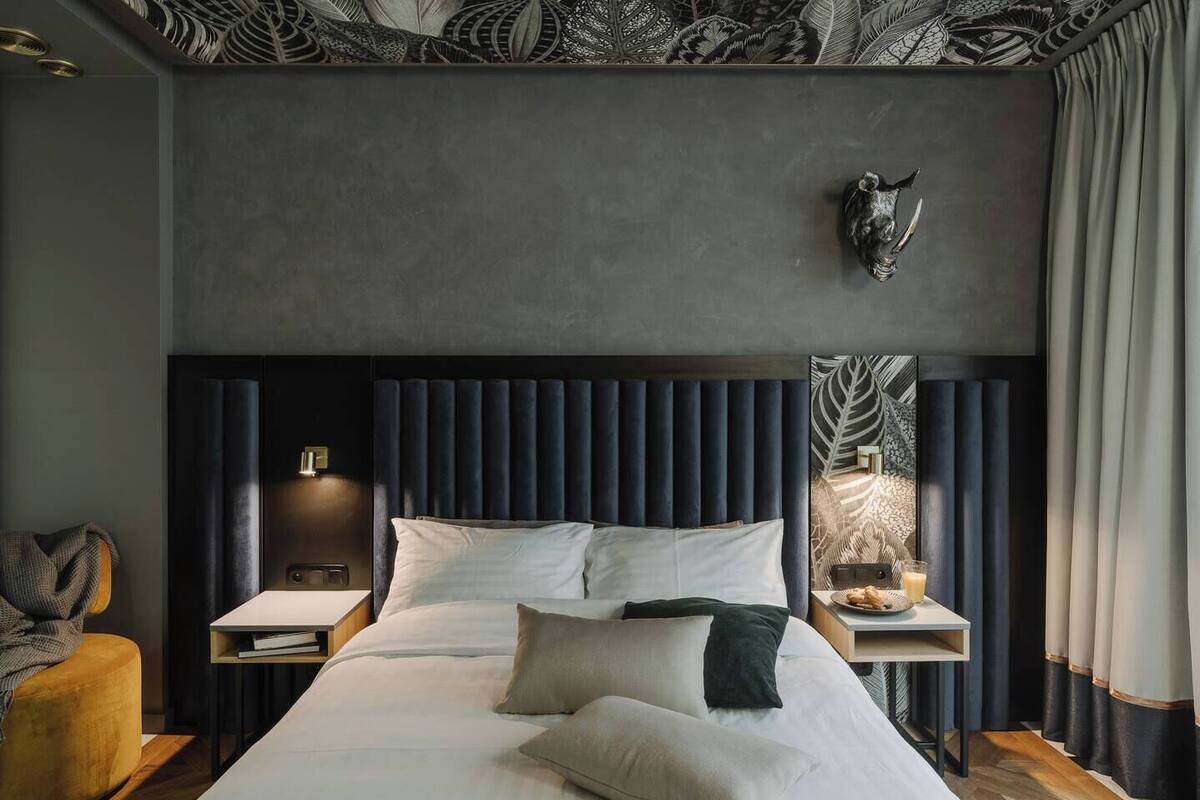 Ein modernes Schlafzimmer mit einem großen Bett, dunkelbraunem Kopfteil, Nachttischlampen und einer dekorativen Wandgestaltung.