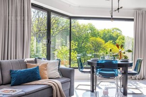 A modern living room with a grey sofa, blue cushions, and a dining table with chairs.